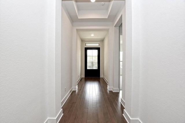 doorway with a textured wall, baseboards, dark wood-style floors, and a raised ceiling