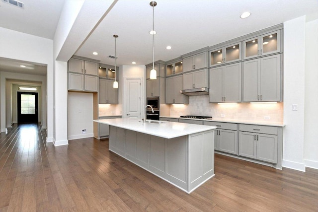 kitchen with under cabinet range hood, a sink, a center island with sink, gray cabinetry, and gas stovetop