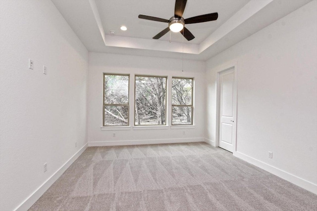 empty room with baseboards, light carpet, a ceiling fan, and a raised ceiling