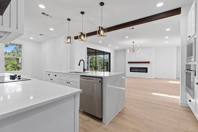 208 Ulupau Cir, Bastrop, TX 78602 - kitchen featuring appliances with stainless steel finishes, a sink, light wood-type flooring, a kitchen island with sink, and white cabinets