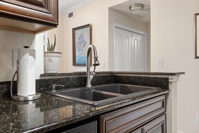 room details featuring dark stone countertops, dark brown cabinets, visible vents, ornamental molding, and a sink