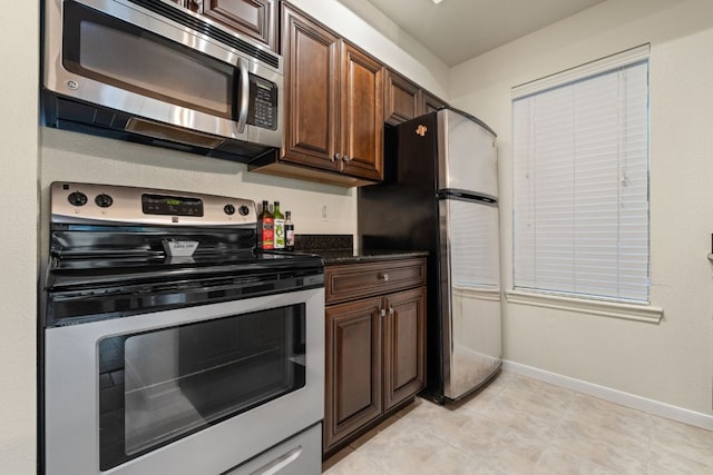 kitchen with dark countertops, baseboards, appliances with stainless steel finishes, and light tile patterned floors
