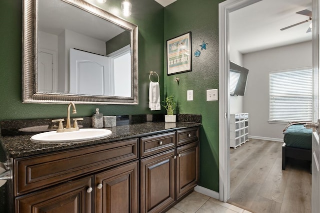 bathroom with wood finished floors, vanity, ceiling fan, a textured wall, and baseboards