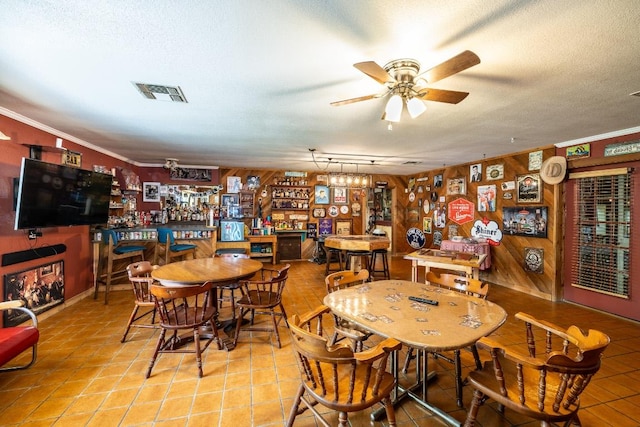 110 Live Oak St, Gonzales, TX 78629 - tiled dining space featuring a dry bar, a textured ceiling, visible vents, a ceiling fan, and wood walls