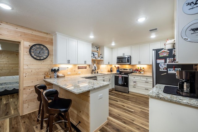 110 Live Oak St, Gonzales, TX 78629 - kitchen featuring wood finished floors, stainless steel appliances, a peninsula, white cabinetry, and visible vents