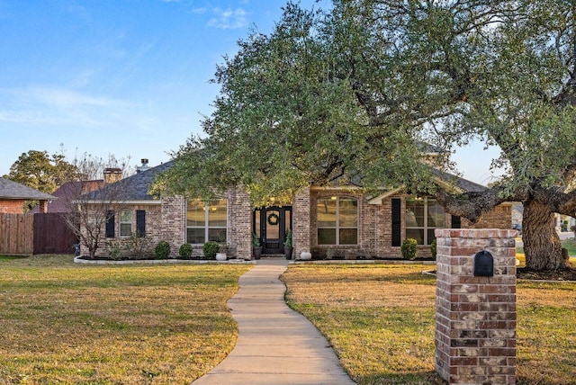 view of front of house with brick siding, a front yard, and fence