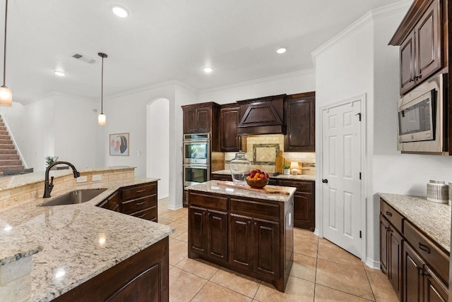 kitchen with a sink, premium range hood, arched walkways, a kitchen island with sink, and appliances with stainless steel finishes