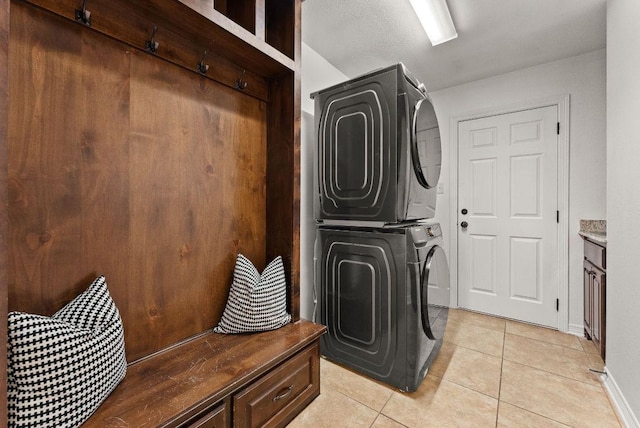laundry room with stacked washer / drying machine, cabinet space, baseboards, and light tile patterned floors