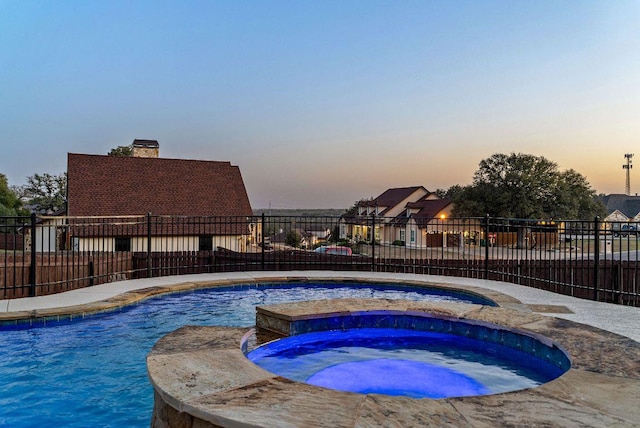 pool at dusk featuring fence and a pool with connected hot tub
