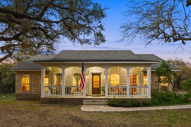 exterior space featuring stone siding, a shingled roof, and covered porch