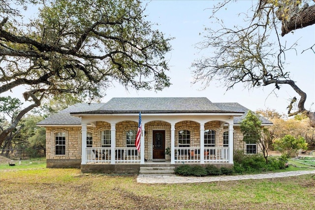 view of front of home with stone siding, a front lawn, covered porch, and fence