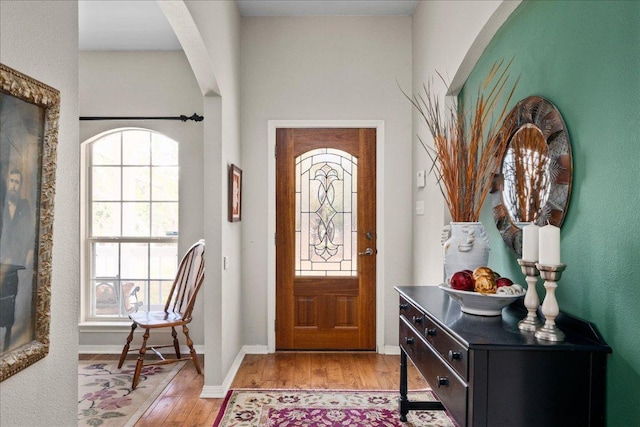 foyer with light wood-style flooring, baseboards, arched walkways, and a healthy amount of sunlight