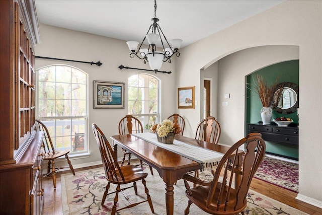 dining area with arched walkways, wood finished floors, baseboards, and a notable chandelier