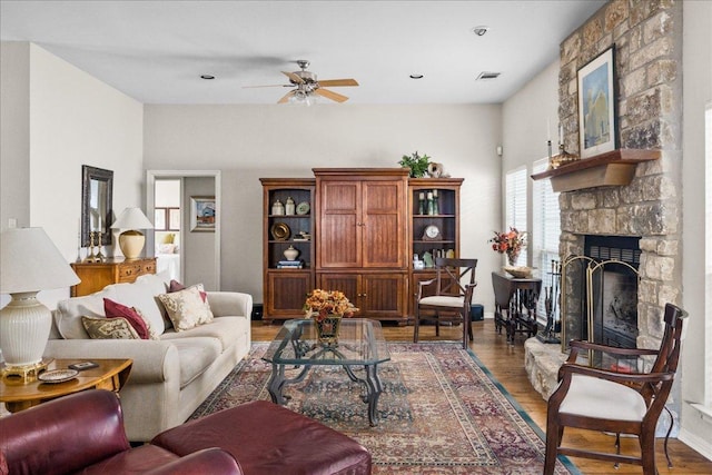 living area with a stone fireplace, visible vents, wood finished floors, baseboards, and ceiling fan