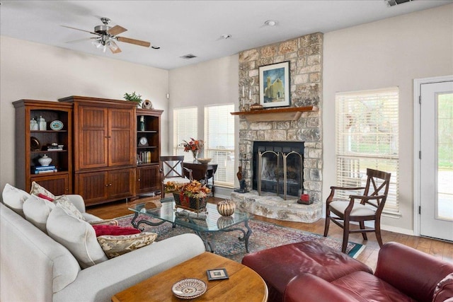 living area with a fireplace, wood finished floors, a wealth of natural light, and a ceiling fan