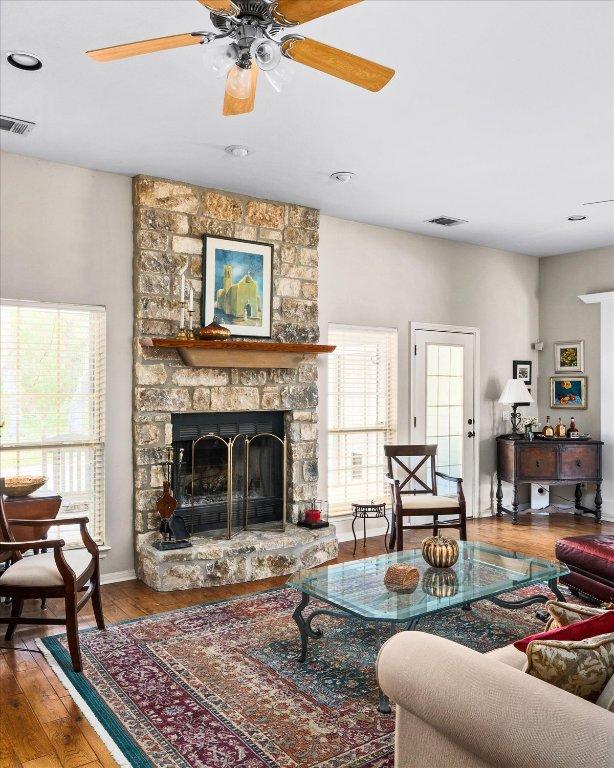 living area with a ceiling fan, wood finished floors, a stone fireplace, and visible vents
