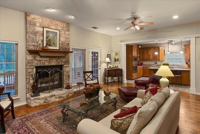 living room with baseboards, a ceiling fan, a stone fireplace, and light wood-type flooring