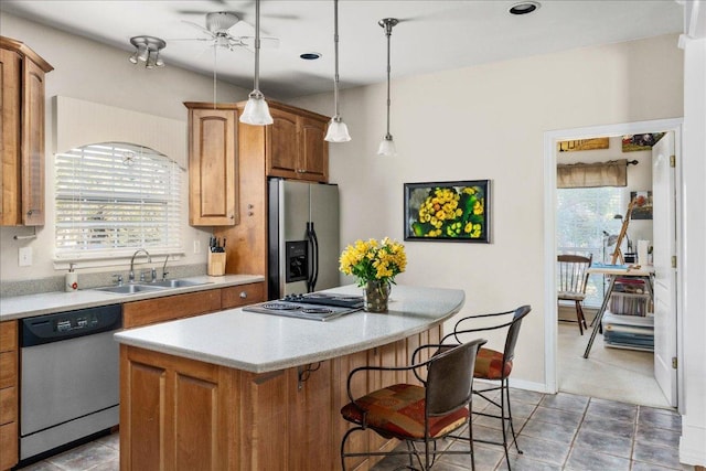 kitchen with a sink, ceiling fan, stainless steel appliances, light countertops, and a kitchen island