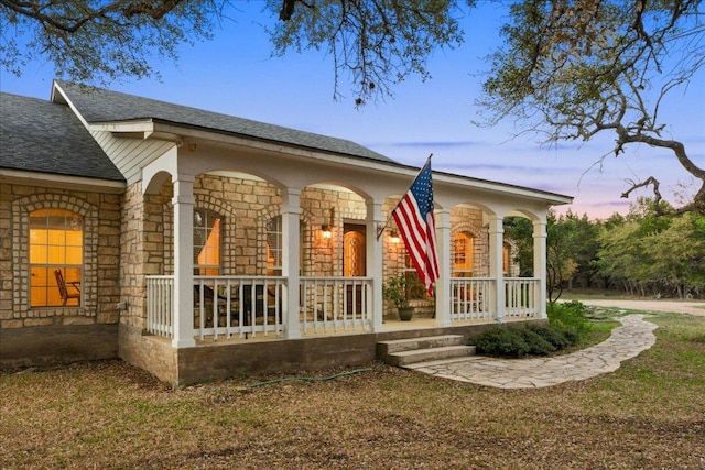 exterior space featuring a porch, roof with shingles, and stone siding