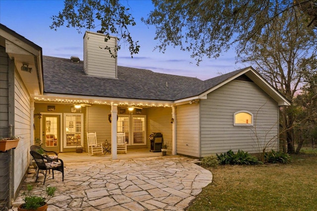 rear view of property with a lawn, a shingled roof, a patio, and a chimney