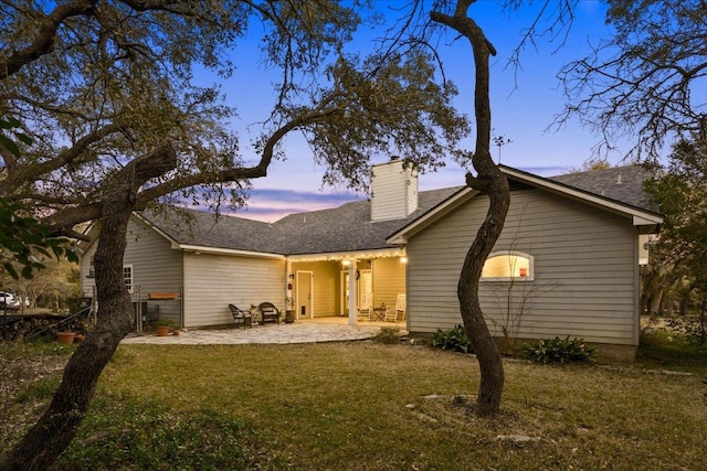 rear view of property featuring a chimney, roof with shingles, a yard, and a patio