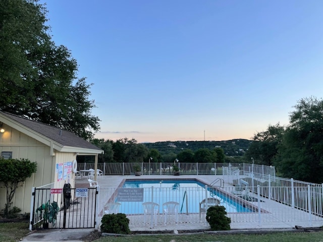 pool at dusk featuring a community pool, a patio area, and fence