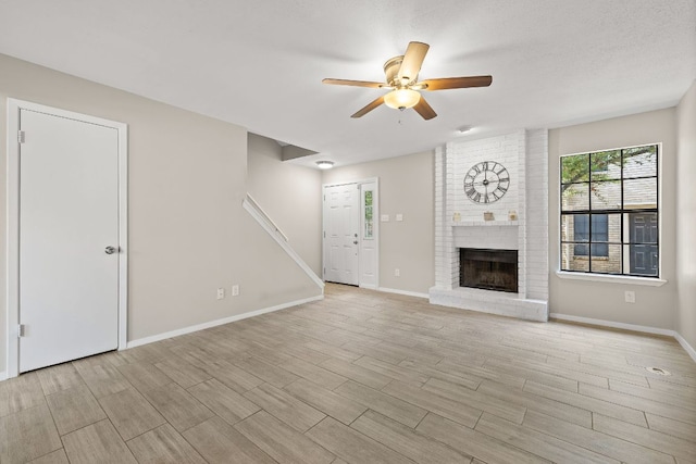 unfurnished living room with ceiling fan, baseboards, light wood finished floors, and a fireplace