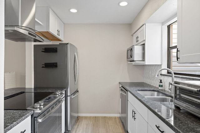 kitchen featuring white cabinets, backsplash, a sink, wall chimney exhaust hood, and appliances with stainless steel finishes