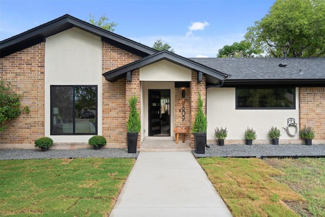 view of front of property featuring a front lawn, brick siding, roof with shingles, and stucco siding
