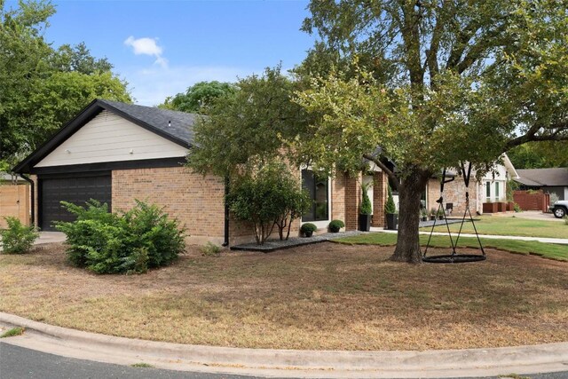 view of property hidden behind natural elements featuring an attached garage, brick siding, and a front yard