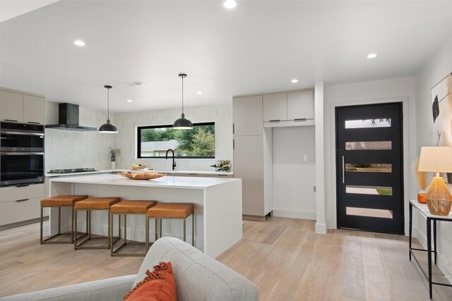 kitchen with cooktop, light wood-style floors, stainless steel double oven, modern cabinets, and wall chimney exhaust hood