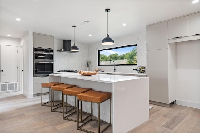 kitchen featuring light wood-style flooring, wall chimney exhaust hood, stainless steel double oven, and gray cabinetry