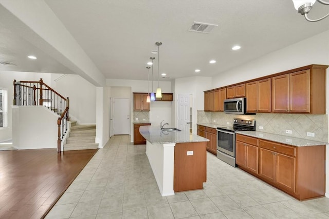 kitchen with stainless steel appliances, a sink, visible vents, brown cabinets, and light stone countertops