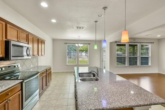 kitchen with a sink, brown cabinetry, stainless steel appliances, a center island with sink, and visible vents