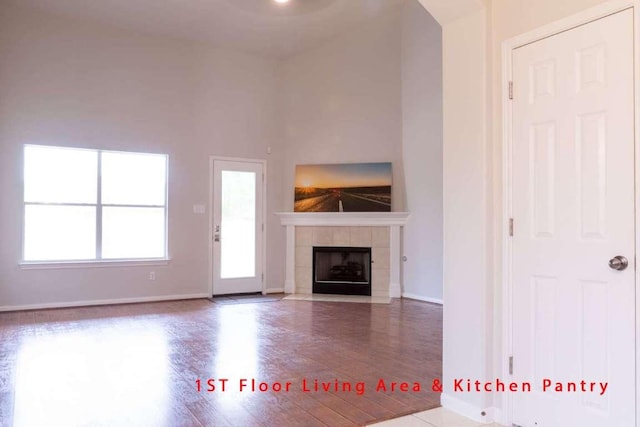 102 Buck Shot Ct, Bastrop, TX 78602 - unfurnished living room with wood finished floors, a tiled fireplace, and baseboards
