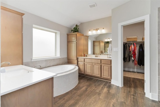 bathroom featuring vaulted ceiling, two vanities, wood finished floors, and a sink