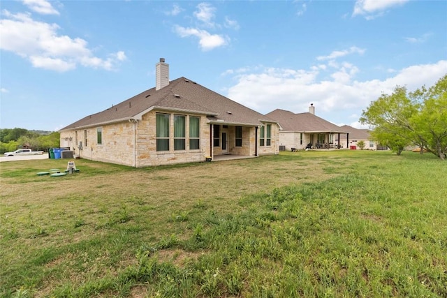 rear view of house with stone siding, a lawn, a chimney, and a patio