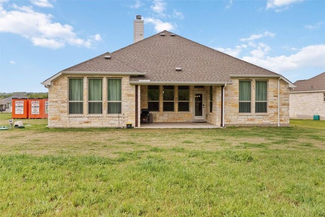 rear view of house featuring stone siding, a chimney, roof with shingles, and a patio