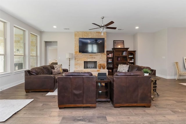 living area with visible vents, baseboards, wood finished floors, ceiling fan, and a stone fireplace