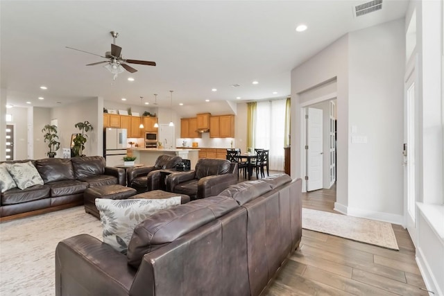 living area with light wood-style flooring, visible vents, recessed lighting, and ceiling fan
