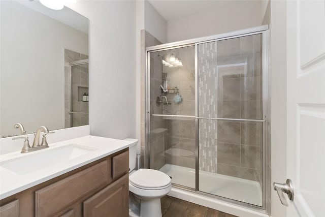 bathroom with a shower stall, toilet, vanity, and wood finished floors