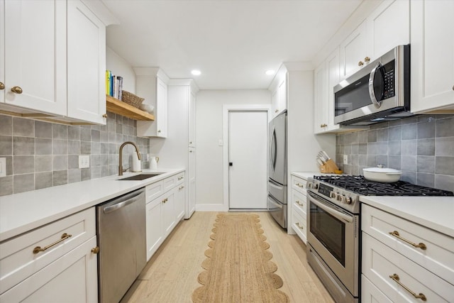 2602 Baxter Dr, Austin, TX 78745 - kitchen featuring appliances with stainless steel finishes, a sink, light wood-type flooring, white cabinetry, and light countertops