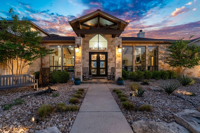 exterior entry at dusk featuring french doors, stone siding, and a chimney