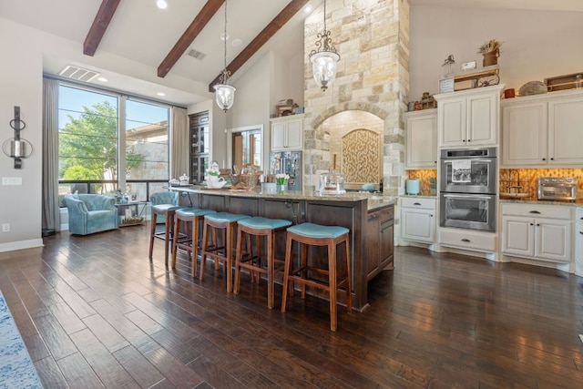 kitchen with high vaulted ceiling, a kitchen breakfast bar, light stone counters, double oven, and backsplash