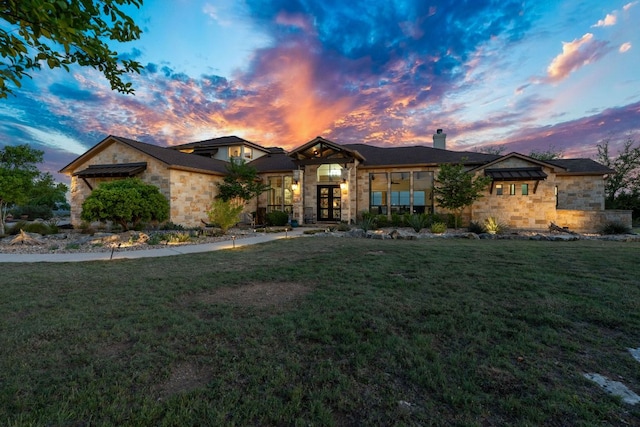view of front of house with french doors, a lawn, stone siding, and a chimney