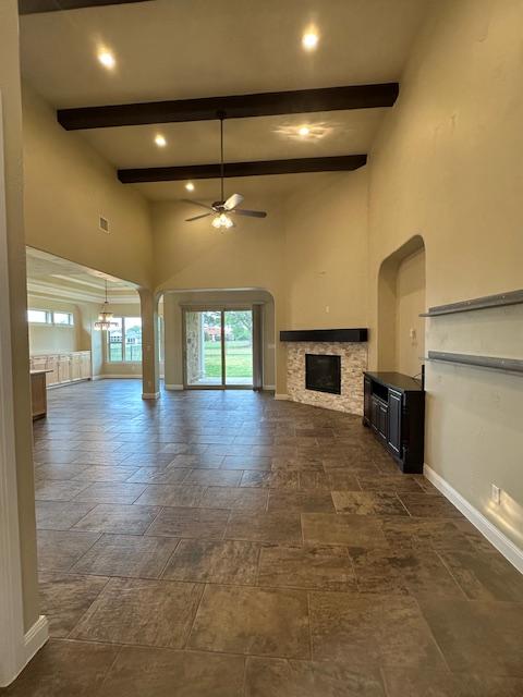 201 Grand Oaks Ln, Georgetown, TX 78628 - unfurnished living room featuring ceiling fan, beam ceiling, a stone fireplace, a towering ceiling, and baseboards