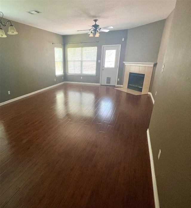 unfurnished living room featuring a tiled fireplace, baseboards, visible vents, wood finished floors, and ceiling fan