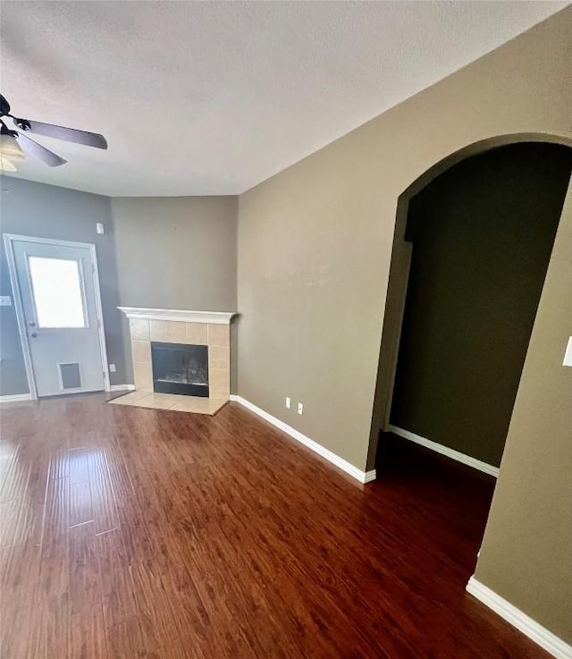 unfurnished living room featuring arched walkways, a ceiling fan, wood finished floors, and a fireplace
