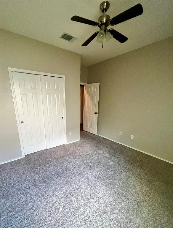 unfurnished bedroom with dark carpet, visible vents, a closet, baseboards, and ceiling fan