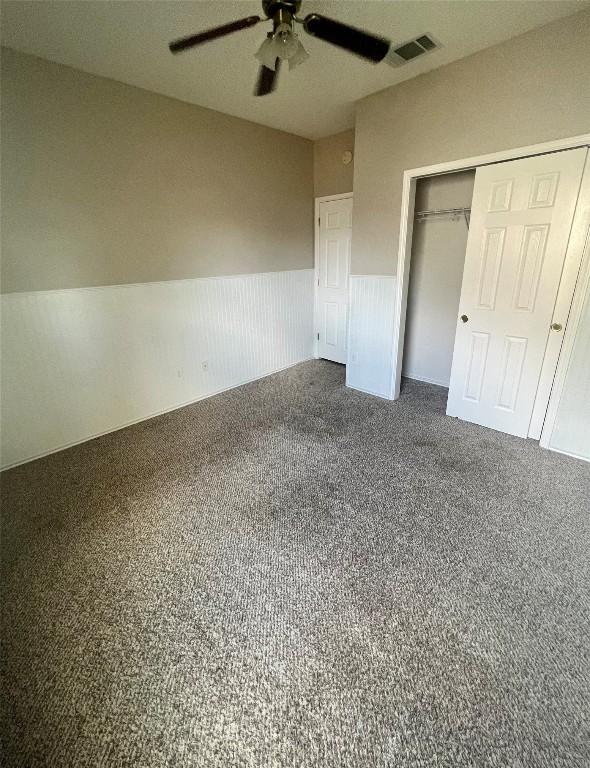 unfurnished bedroom with a closet, wainscoting, ceiling fan, carpet floors, and visible vents
